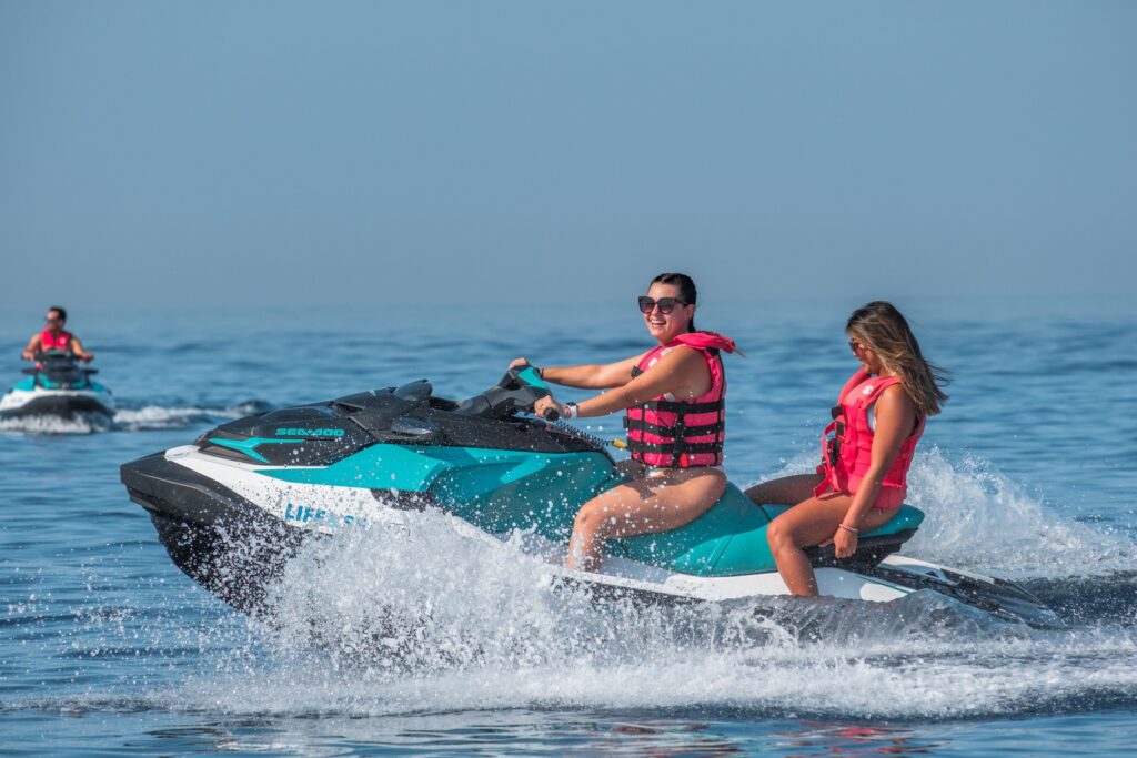 Jet Ski Playa de Palma, Two people wearing red life jackets enjoying an exciting jet ski ride, speeding over the clear waters at Playa de Palma, Mallorca. 