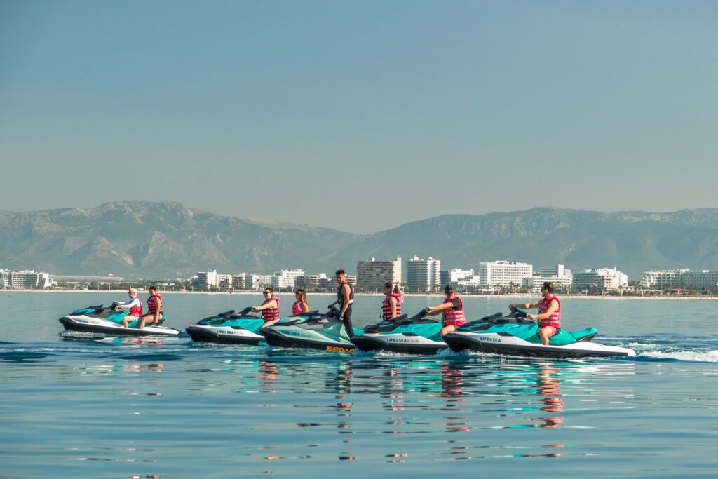Jet Ski Playa de Palma 
, Group of people riding jet skis on the calm, turquoise waters at Playa de Palma, Mallorca, with the beach promenade and mountains in the background.