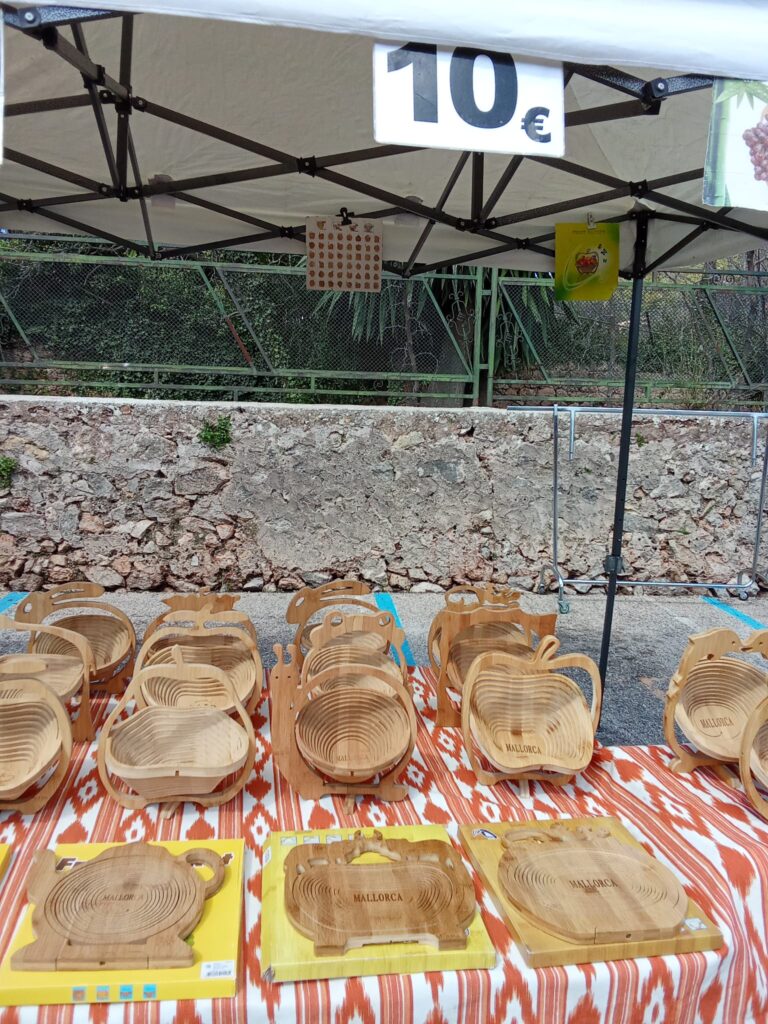 A market stall selling intricately designed wooden folding baskets and cutting boards with "Mallorca" engravings.
