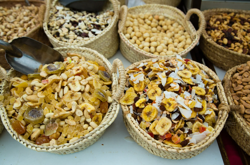 A colorful selection of dried fruits, including pineapple, mango, kiwi, papaya, and dates, is neatly arranged in trays at a market stall in Pollença, offering a variety of sweet and tangy flavors.