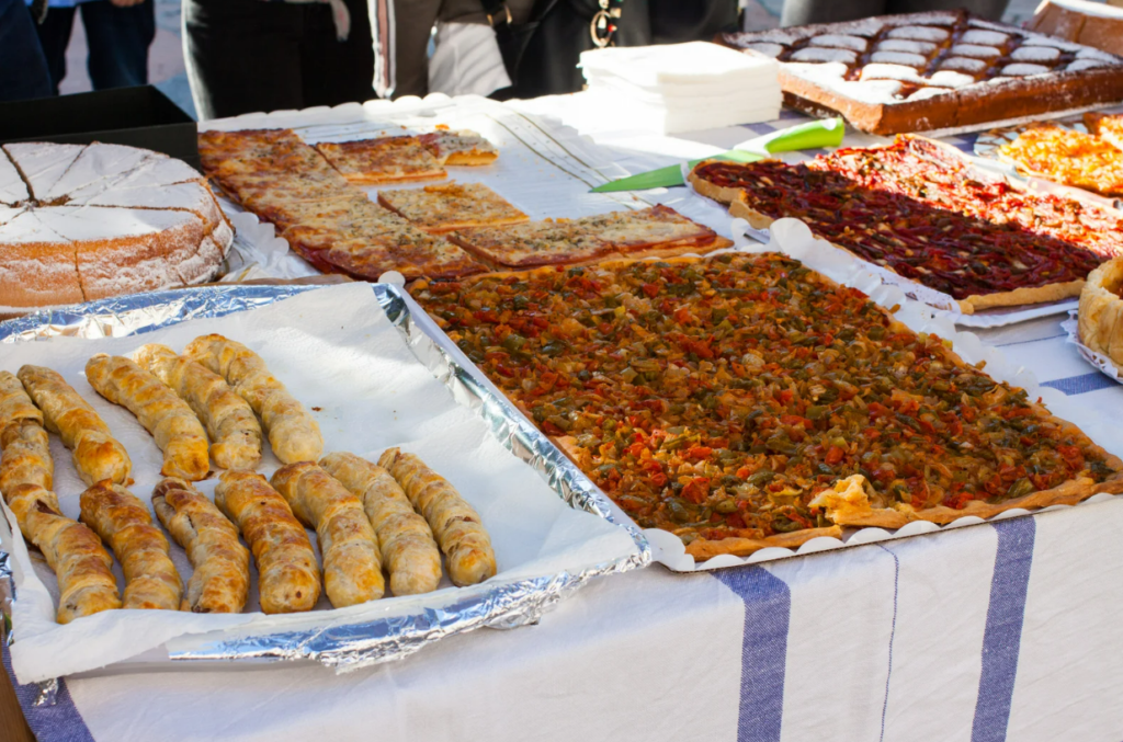 A market stall in Porreres, Mallorca, displays an assortment of traditional baked goods, including flaky vegetable coca, puff pastry rolls, and sugar-dusted sponge cakes, offering a delicious taste of local cuisine.