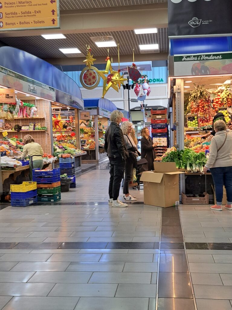A lively scene inside Mercat de l'Olivar, with shoppers exploring the fresh food stalls under colorful Christmas decorations.