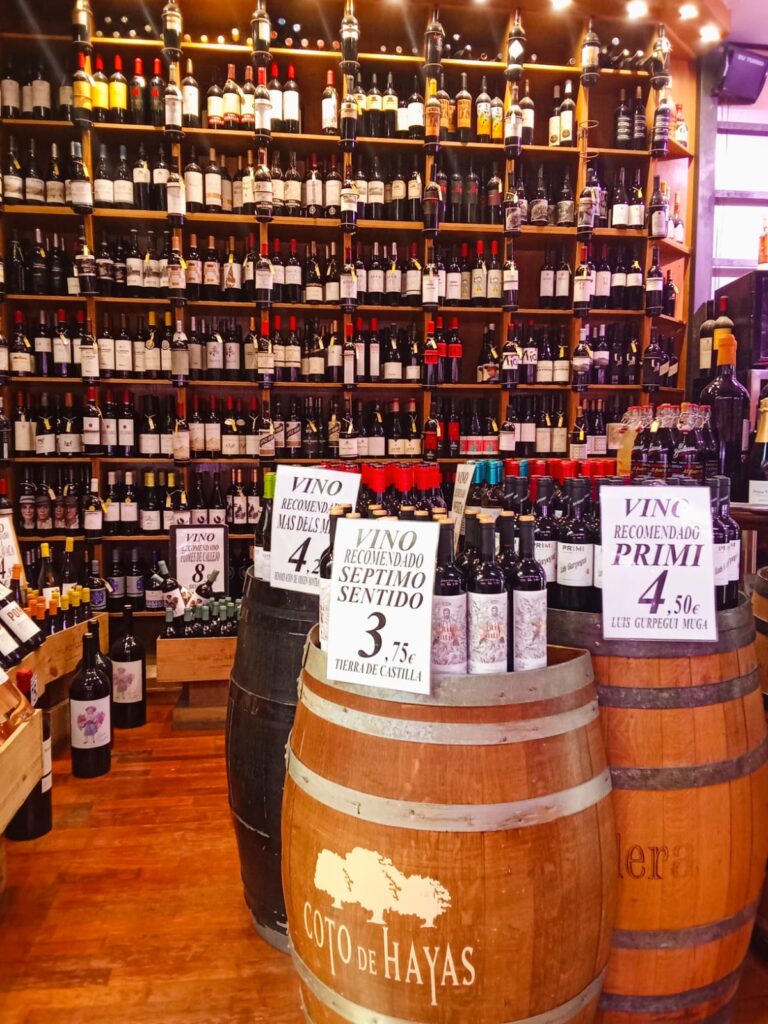 Wine bottles lined up on wooden barrels at a wine stall in Mercat Pere Garau.