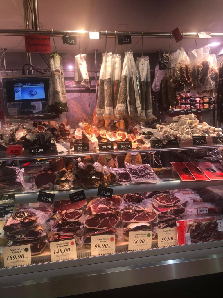 A gourmet butcher's stall displaying premium Jamón Ibérico and other cured meats at Mercat Santa Catalina in Palma de Mallorca.
