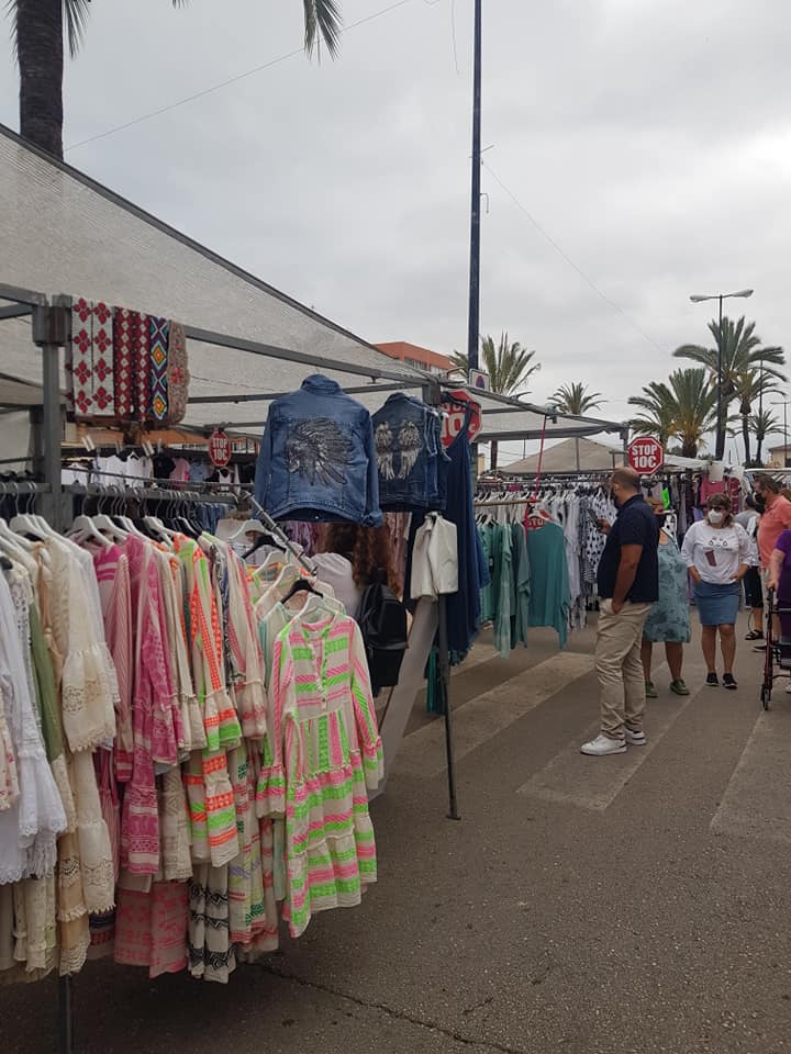 People shopping for dresses, textiles, and beachwear at the Weekly Market Arenal, Mallorca, surrounded by local street vendors.