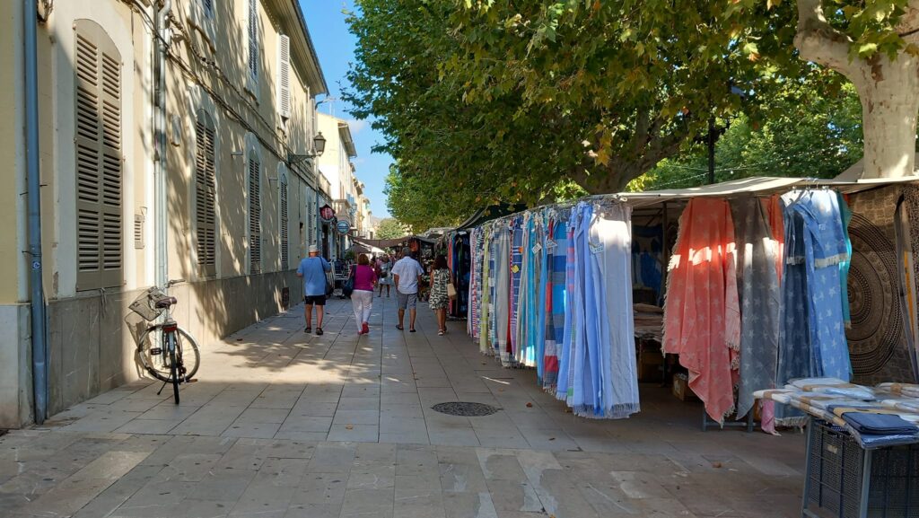 A shaded market street lined with textile stalls, offering handcrafted scarves, shawls, and fabrics.