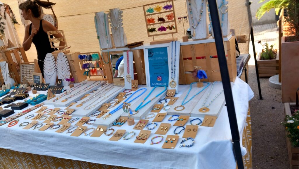 A jewelry stall at a weekly market Arta in Mallorca displaying handmade necklaces, bracelets, and earrings in Mediterranean colors.