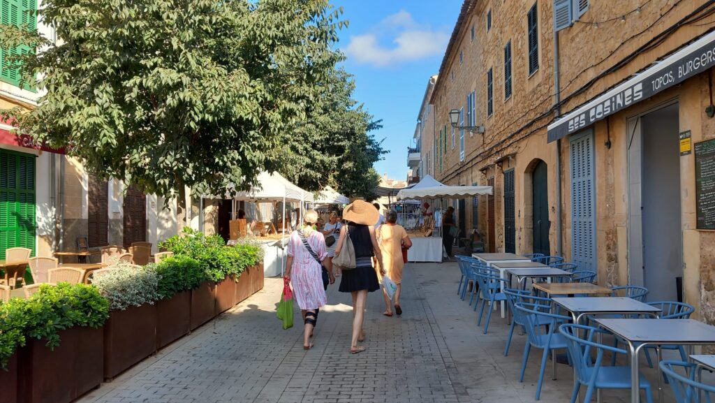 Shoppers strolling through a charming market street, surrounded by artisan stands and cozy cafés in Mallorca.