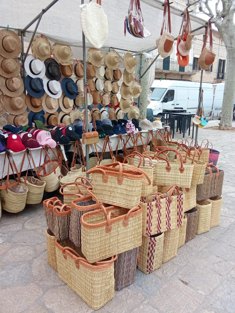 A colorful market stall at the Binissalem weekly market, displaying handcrafted straw hats, woven bags, and stylish accessories.