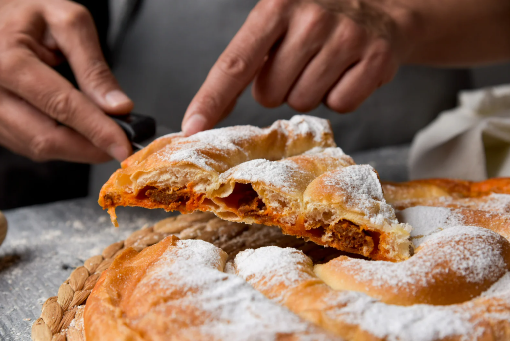 Freshly baked ensaimada being sliced at the weekly market in Cala Millor, Mallorca – a sweet symbol of Mallorcan tradition.