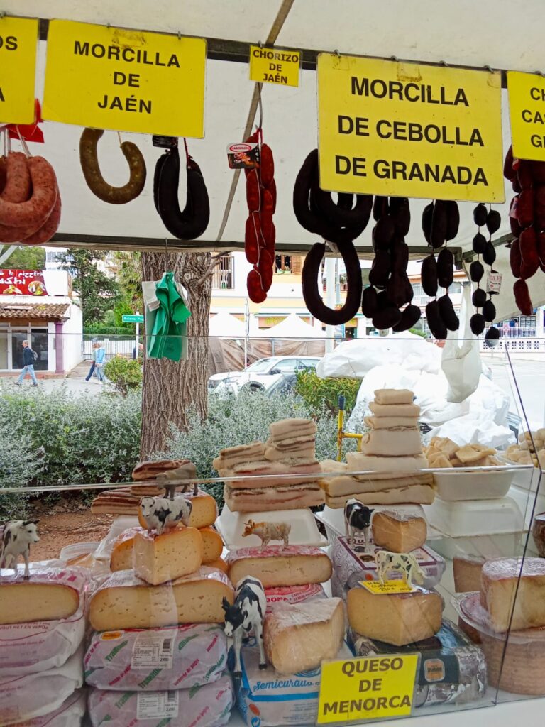 Traditional Spanish sausages like morcilla and chorizo, along with cheeses from Menorca, on display at the Weekly Market Paguera – authentic flavors of the region.