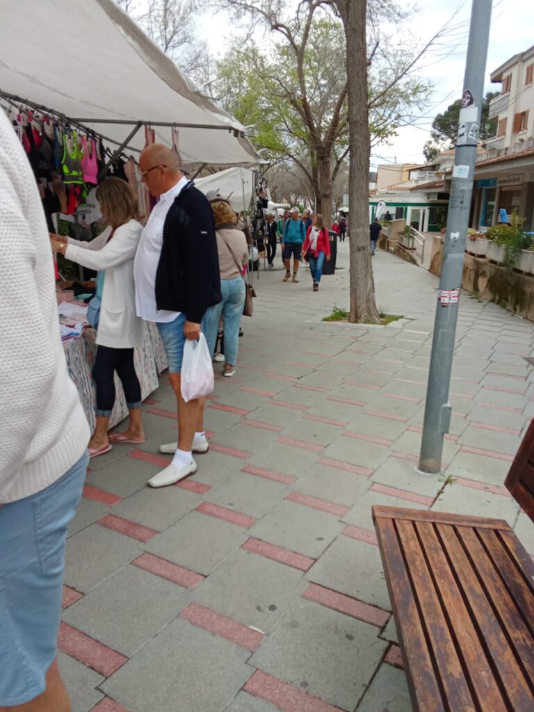 Shoppers exploring various stalls at the Weekly Market Paguera, Mallorca, surrounded by local vendors, trees, and a relaxed village vibe.