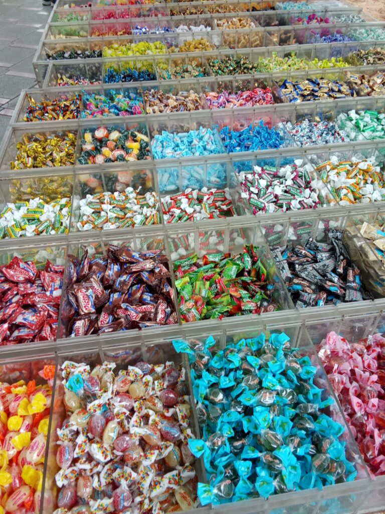 Wide selection of colorful candies and sweets sorted in transparent boxes at the Weekly Market Paguera – a vibrant treat for young and old alike.
