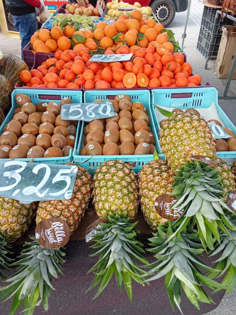 A colorful fruit stall at the Weekly Market in Santa Ponsa, Mallorca, featuring pineapples, kiwis, oranges, and other fresh produce.