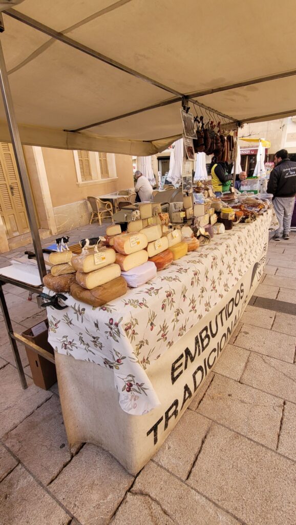A cheese and sausage stall at the Weekly Market Santanyí, featuring a selection of traditional Mallorcan delicacies.