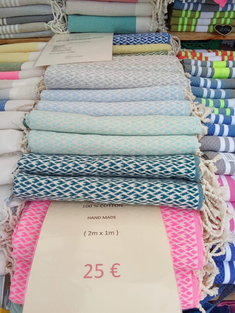 Handmade 100% cotton towels in soft pastel colors neatly rolled and stacked at a Sóller market stall, each measuring 2m x 1m and priced at €25.