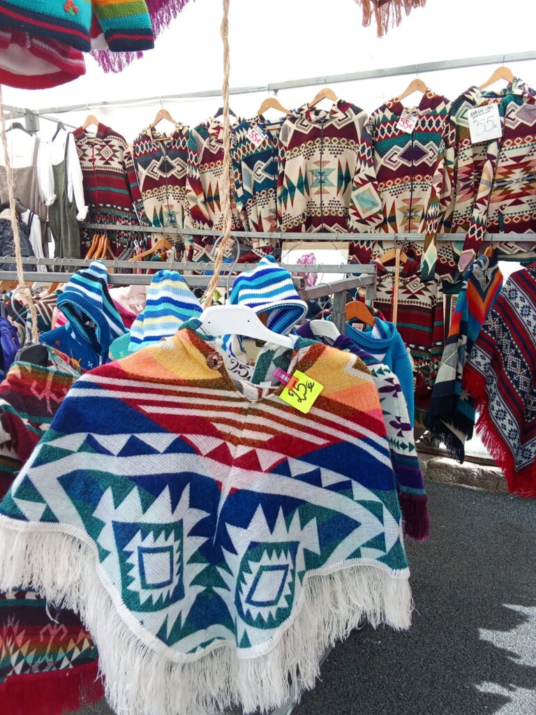 Traditional ponchos and patterned zip-up jackets with Aztec-style designs hanging at a market stall in Sóller, Mallorca, with visible prices from €25 to €55