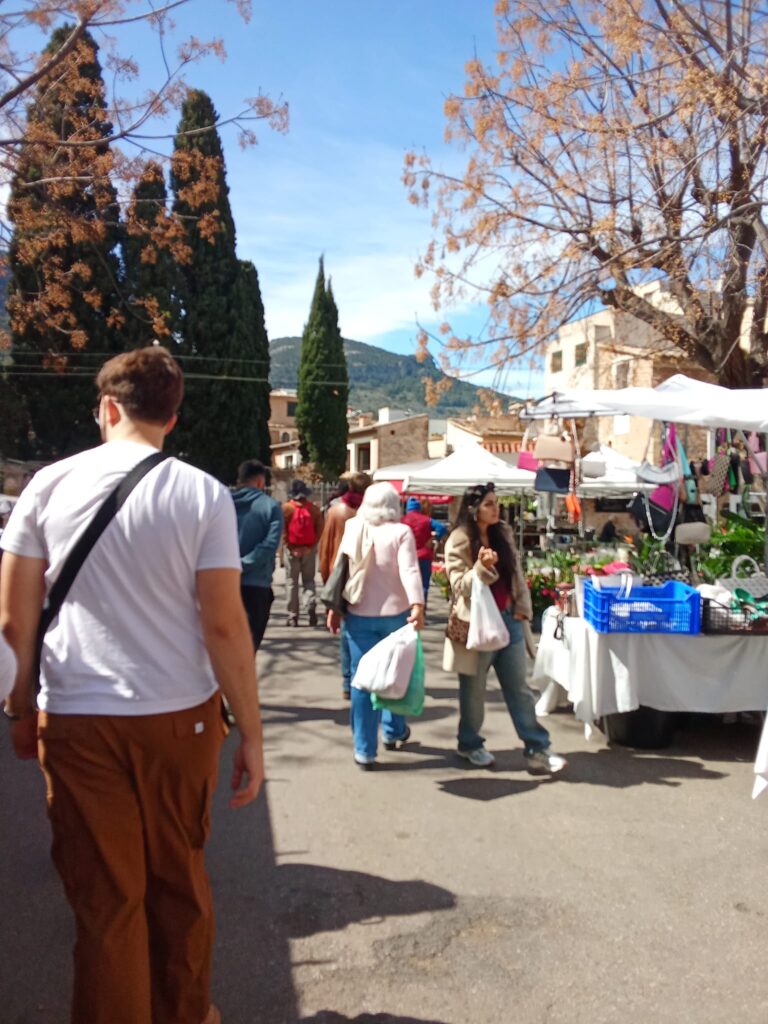 Vibrant hand-painted Mallorcan ceramics including jugs, cups, bowls, and decorative pieces with floral motifs, displayed on a woven mat at the Sóller market