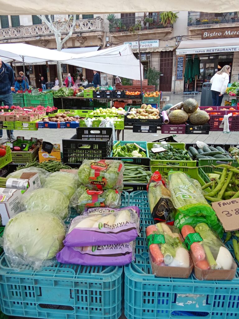 The weekly market Llucmajor, Mallorca, offers a vibrant mix of fresh local produce, traditional cured sausages, artisanal cheeses, handmade ceramics, and clothing stalls, set against the charming backdrop of the town’s historic streets and plazas.