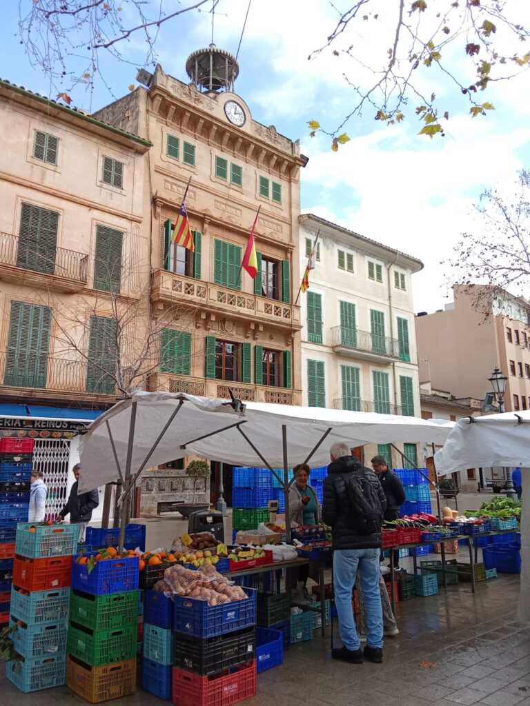 The weekly market Llucmajor, Mallorca, offers a vibrant mix of fresh local produce, traditional cured sausages, artisanal cheeses, handmade ceramics, and clothing stalls, set against the charming backdrop of the town’s historic streets and plazas.