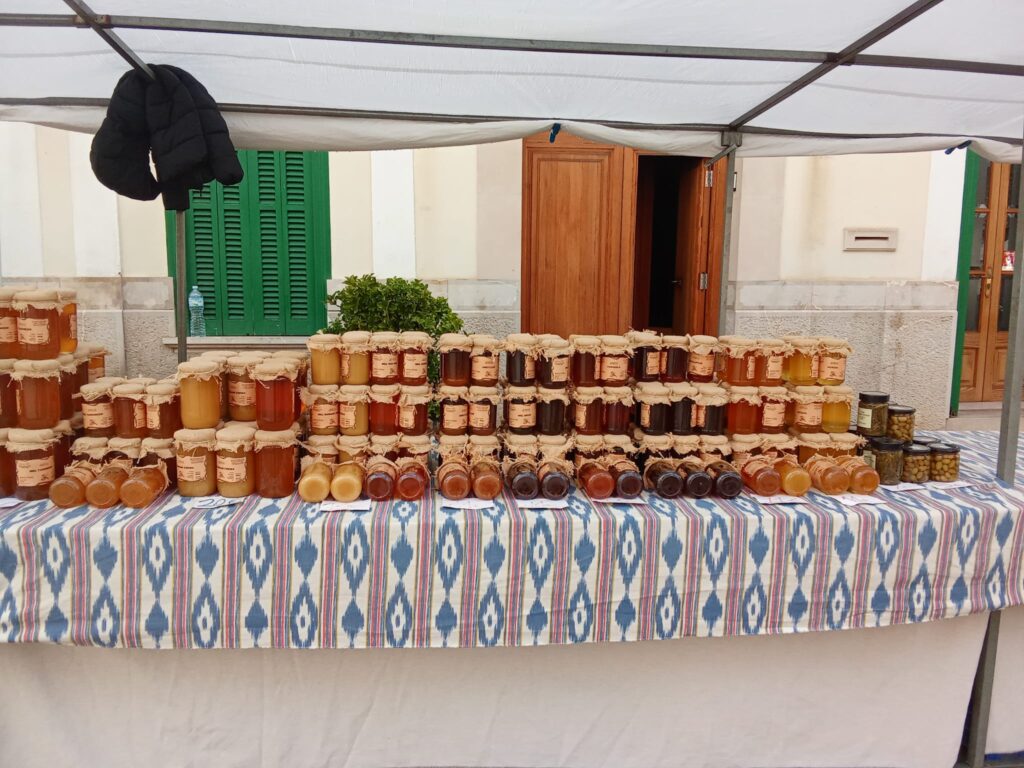 The weekly market Llucmajor, Mallorca, offers a vibrant mix of fresh local produce, traditional cured sausages, artisanal cheeses, handmade ceramics, and clothing stalls, set against the charming backdrop of the town’s historic streets and plazas.