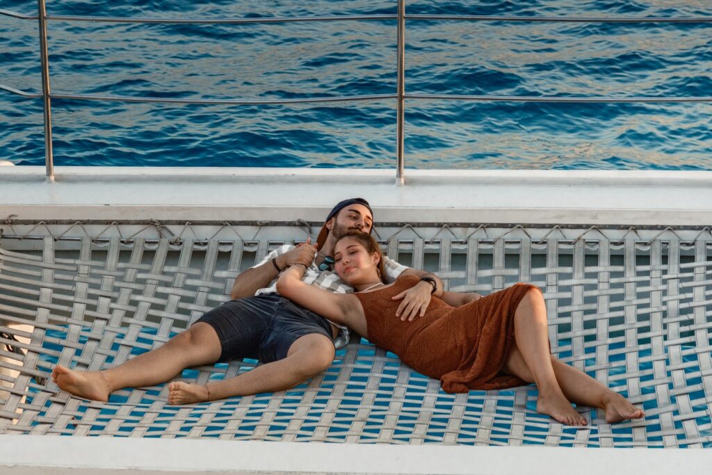 Couple relaxing on the net of a catamaran during a romantic sunset cruise in Playa de Palma, Mallorca – pure bliss on the Mediterranean waves.