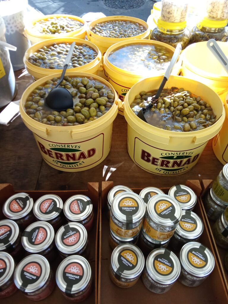Buckets of marinated olives and jars of preserved vegetables at the weekly market in Manacor, Mallorca – showcasing Mediterranean culinary traditions.